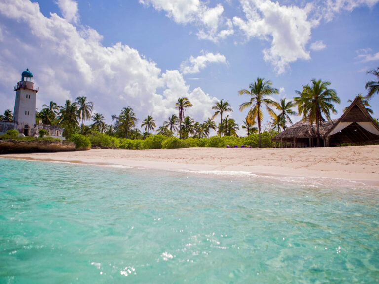 witte vuurtoren aan het witte strand op het onbewoonde eiland Fanjove met alleen een lodge. Grote palmbomen met daaronder struikgewas en een gebouw in bruin