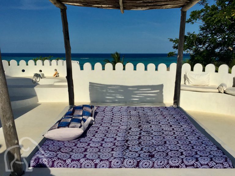 wit dakterras met twee persoons ligbed met afdakdak kijkend over de indische oceaan op Zanzibar