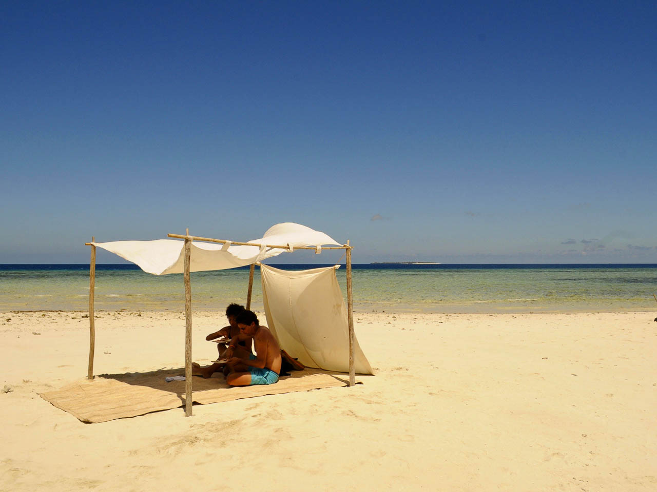 Romantisch lachen op het strand. Twee pas getrouwde mensen zitten onder een een luifel op een leeg strand uitkijkend over de indische oceaan op Fanjove eiland Tanzania