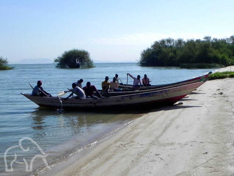 op het strand bij lake victoria met twee boten en vissers daarin die zich klaarmaken het meer op te gaan