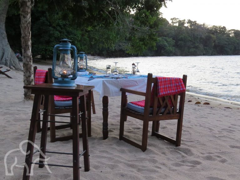 op het strand een gedekte tafel met stoelen klaar voor een romantisch diner aan het het lake victoria