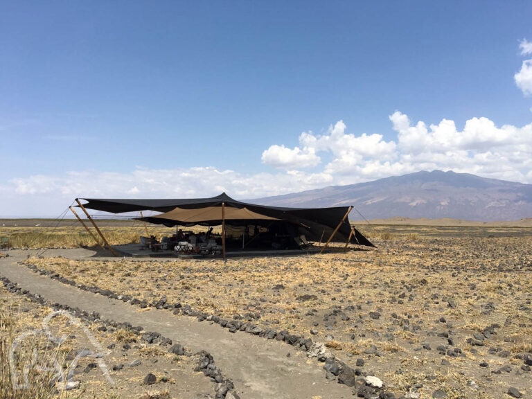 in maandmanschap achtige omgeving bij Lake Natron een open tent met groot schaduwdoek wat dienst doet als restaurant voor een lodge