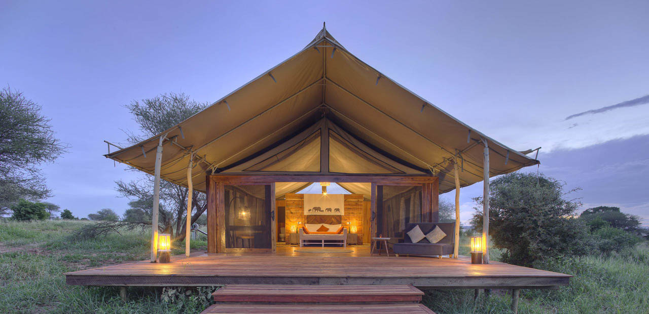 vooraanzicht van een luxe grote safari tent met luifel op een platvorm van hout en verlicht met kaarsjes