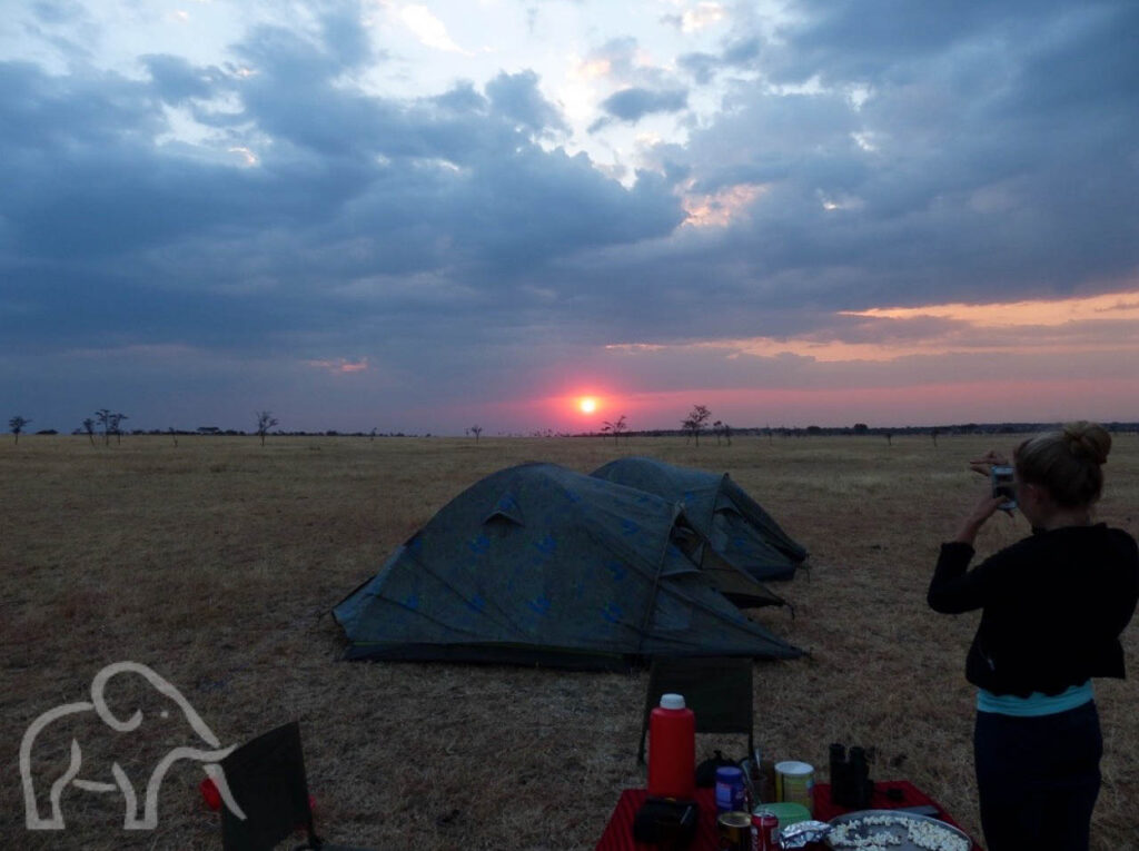 zonsopkomst serengeti met meisje die foto daarvan maakt met twee koepeltentjes op de achtergrond