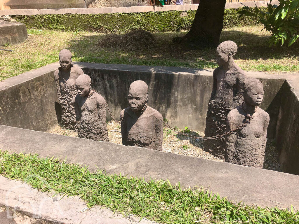 slavernij monument open graf met half uitstekend staande stenen mensen met kettingen om hun nek museum zanzibar tanzania