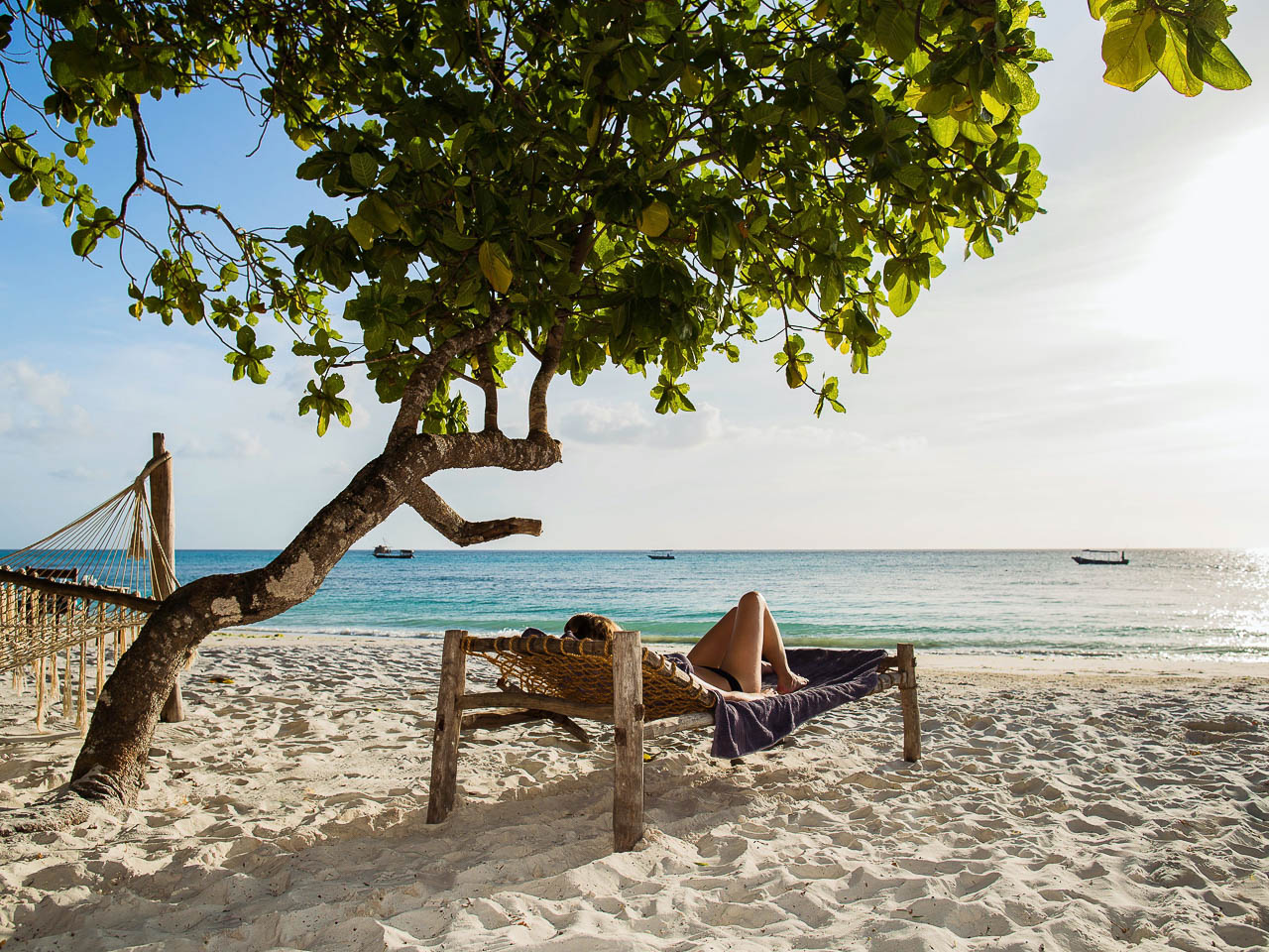 zandstrand op pemba met een ligstoel met daarop iemand onder een boom aan de indische oceaan in tanzania