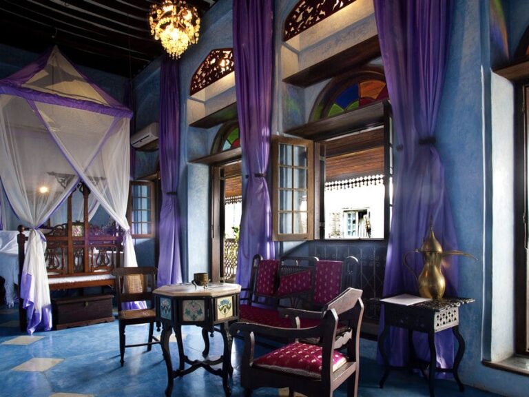 hotelkamer helemaal in het blauw met een groot bed en klamboe opengelaten ramen en houten traditioneel meubilair oosterse sfeer emerson spice hotel zanzibar