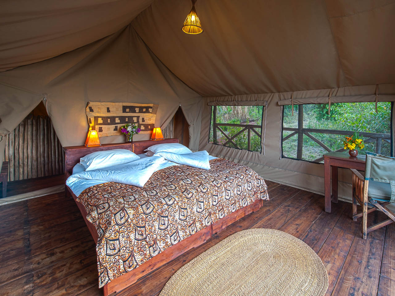 Tanzania safari. Accommodaties. Luxe accommodatie in twee persoons canvas tent met veel authentieke Tanzaniaanse materialen van hout en riet. De tent staat op een houten vloer op palen. In het midden is er een mooi opgemaakt bed.