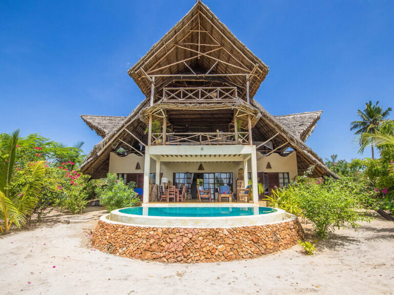 net op het strand een rond zwembad en villa gebouwd met houten palen een schuin rieten dak met drie verdiepingen tussen het groen op Zanzibar