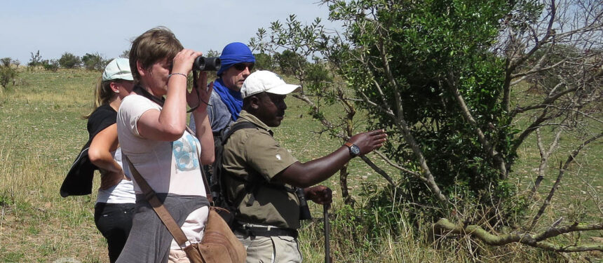 een meerdaagse wandelsafari waarbij een vrouw met verrekijker en gids die wijst en man die luistert op de vlakte van de serengeti