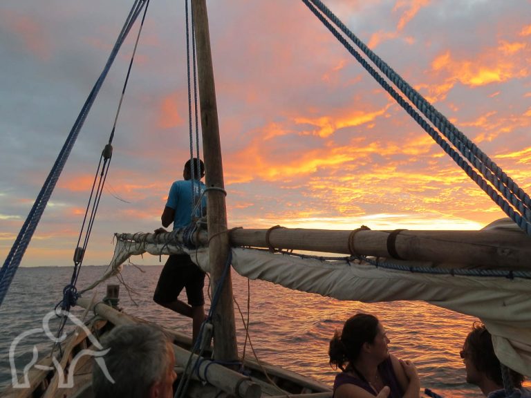 originele dhow, vissersboot, met mast waar man tegenaan staat en mensen in de boot voor een sunset cruise mafia eiland