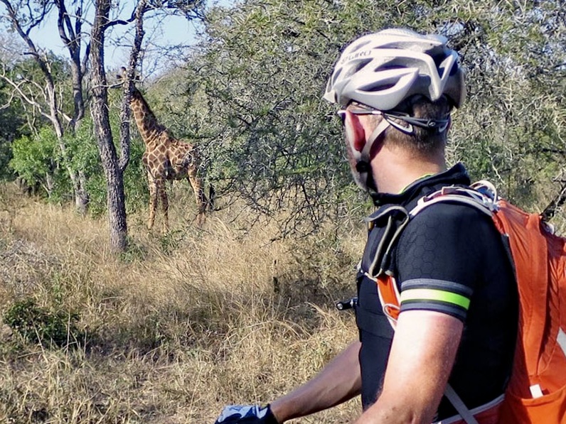 man met helm stilstaand kijken naar een giraffe in het bos bij arusha national park tanzania