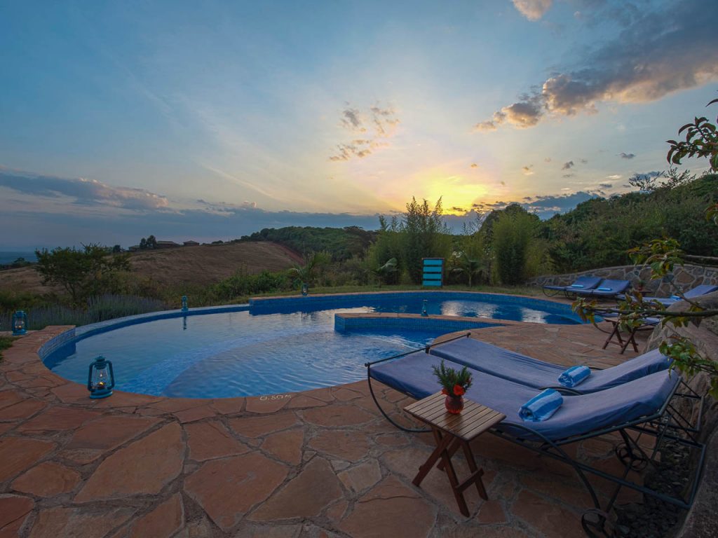 ovaal zwembad met ligbedden erom heen en een ondergaande zon bij rhotia valley lodge tanzania