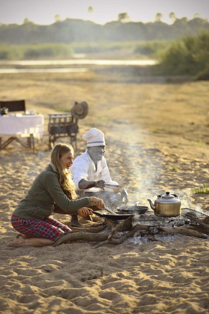 zittende vrouw met kok bij kampvuur tijdens fly camping kickaka meerdaagse luxe wandelsafari ruaha tanzania