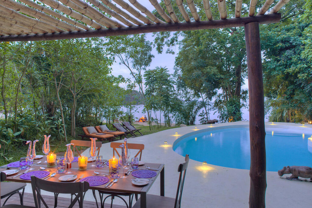 tafel mooi gedekt met kaarsjes aan het zwembad voor een privé diner met op de achtergrond een kampvuur en lake victoria rubondo romantisch huwelijksreis