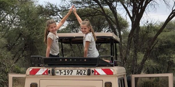 twee lachende jonge kinderen met high five zitten op het dak van de safari auto safari met jonge kinderen