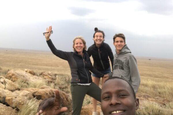 zwaaiende moeder met oudere meisje en jongen met op de voorgrond de gids op de vlaktes van de serengeti tanzania