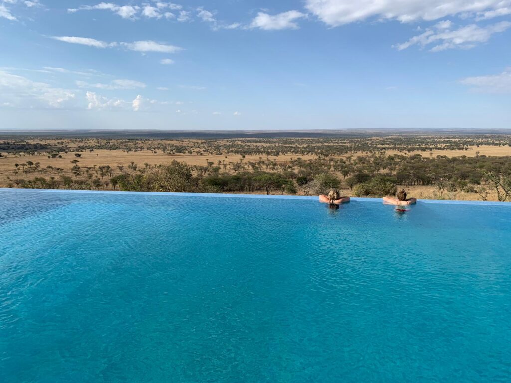 infinity pool zwembad met twee mensen erin uitkijkend over de serengeti vlakte kubu kubu tanzania