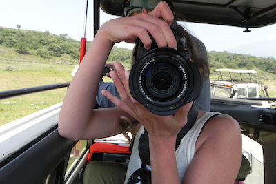 Foto safari Tanzania. Vrouw met camera voor haar hoofd in een safari auto met open dak.