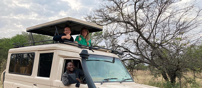Net getrouwd stel staand in de safari auto met dak omhoog en gids achter het stuur tijdens huwelijksreis door tanzania