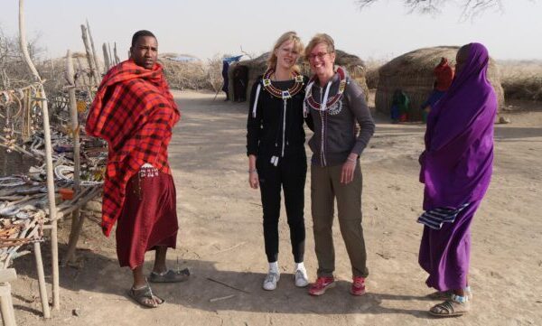 mensen op een excursie in een Masai dorpje met twee masai in felgekleurde kleding