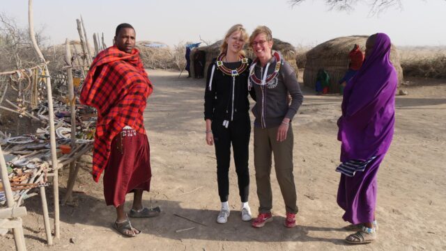 mensen op een excursie in een Masai dorpje met twee masai in felgekleurde kleding