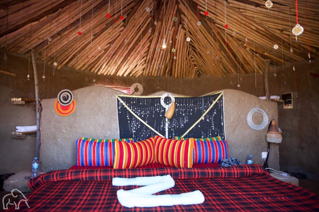 opgemaakt bed in een masai lodge. wwitte lakens en felgekleurde dekens en overal kraaltjes tanzania