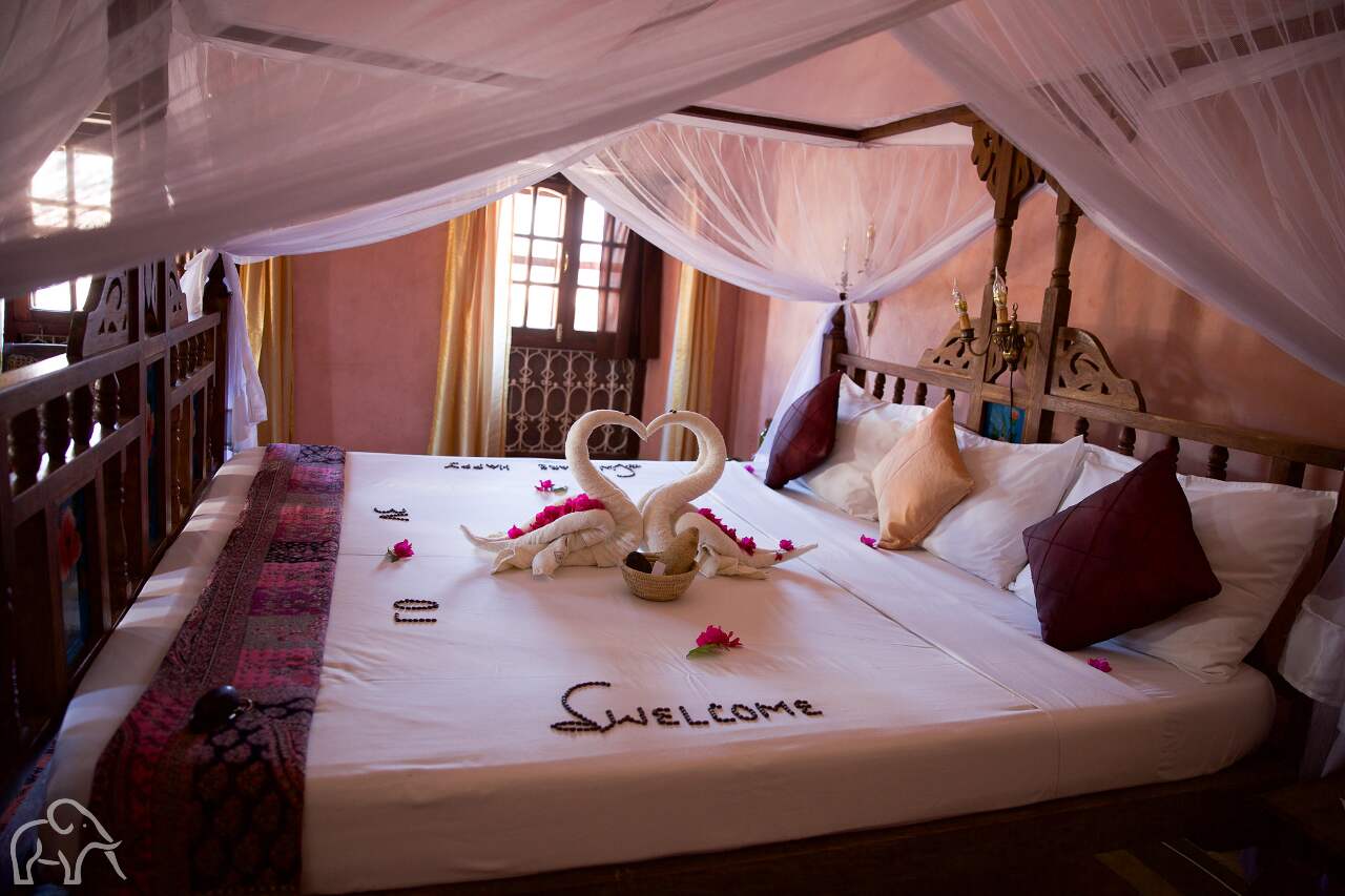 Honeymoon suite Tanzania Huwelijksreis. Mooi opgemaakt bed met handdoeken gevouwen in de vorm van twee zwanen. Welcome gemaakt van roze blaadjes in lodge op Zanzibar