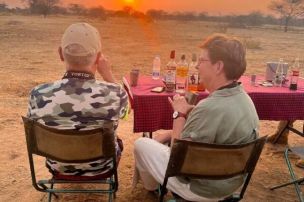 zittende man en vrouw tijdens een sundowner met een lekker drankje en een ondergaande zon in Ruaha national park tanzania