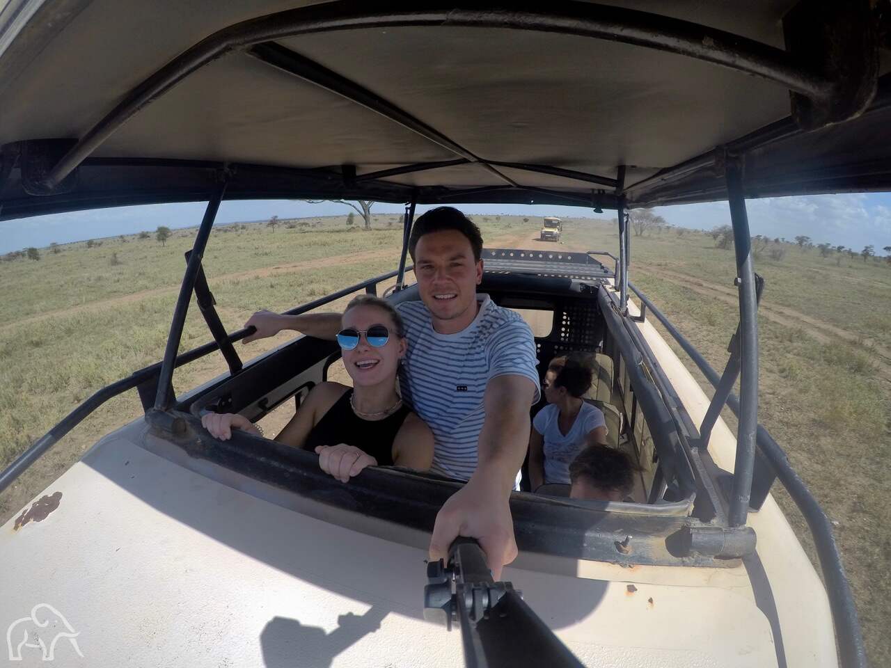 twee gasten van droomreis tanzania die staan in een safari auto met het dak open tijdens een gamedrive op de serengeti