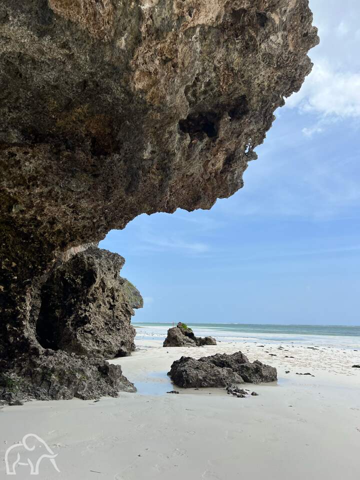 Safari Tanzania reizen ter inspiratie. Op Zanzibar vanaf het witte strand is een grote rots met daarachter de azuur blauwe wateren van de Indische oceaan.