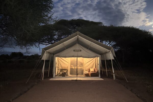 grote safari tent van voren met de lichten binnen aan en twee stoelen ervoor