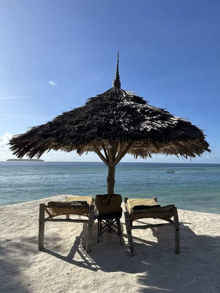 rieten ronde parasol met daaronder twee ligbedden op het parelwitte strand van zanzibar met uitzicht op de indische oceaan