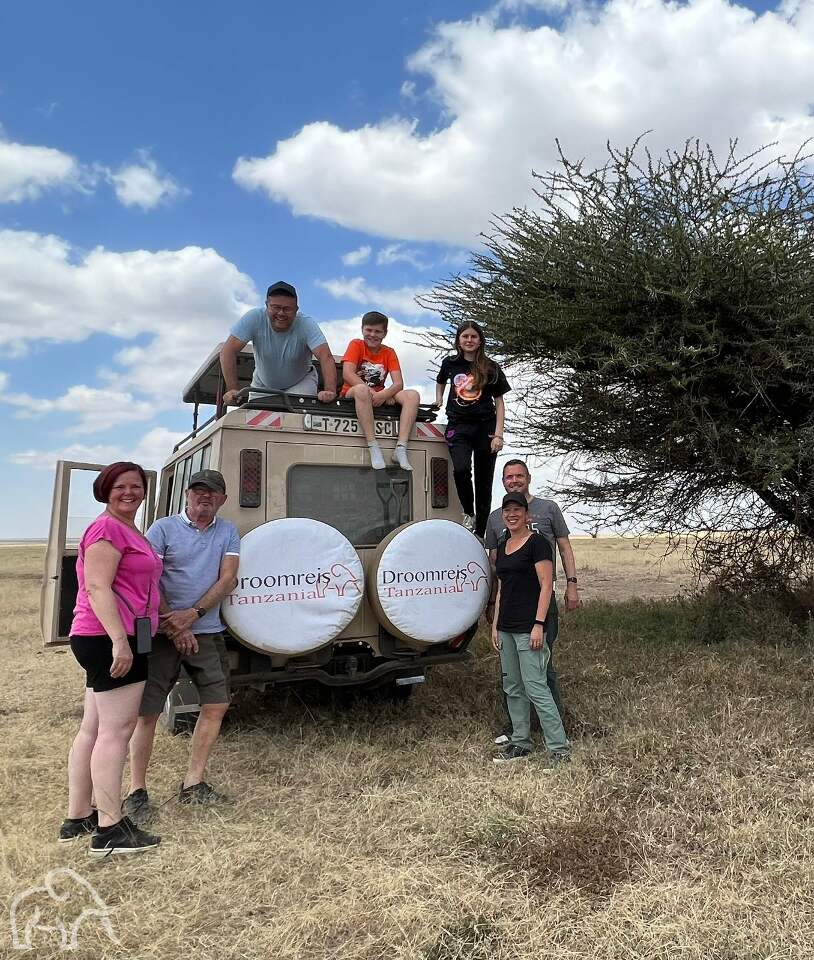 7 reizigers die op safari zijn en in, op en achter de auto van droomreis Tanzania staan