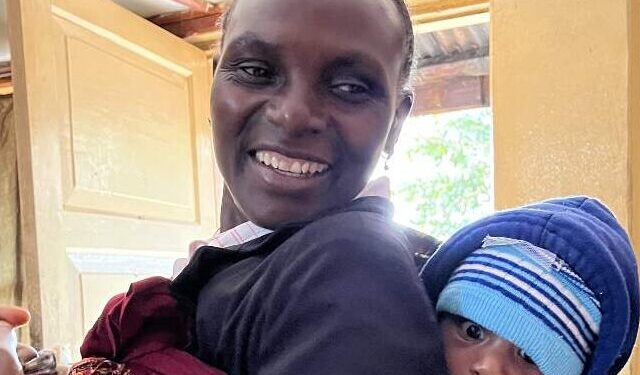 lachende Tanzaniaanse vrouw met een baby op haar rug gebonden