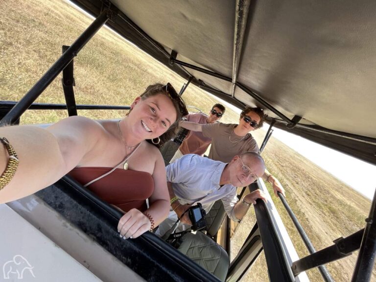 selfie van een familie die op safari is en onder het open dak staan met daarachter de Serengeti