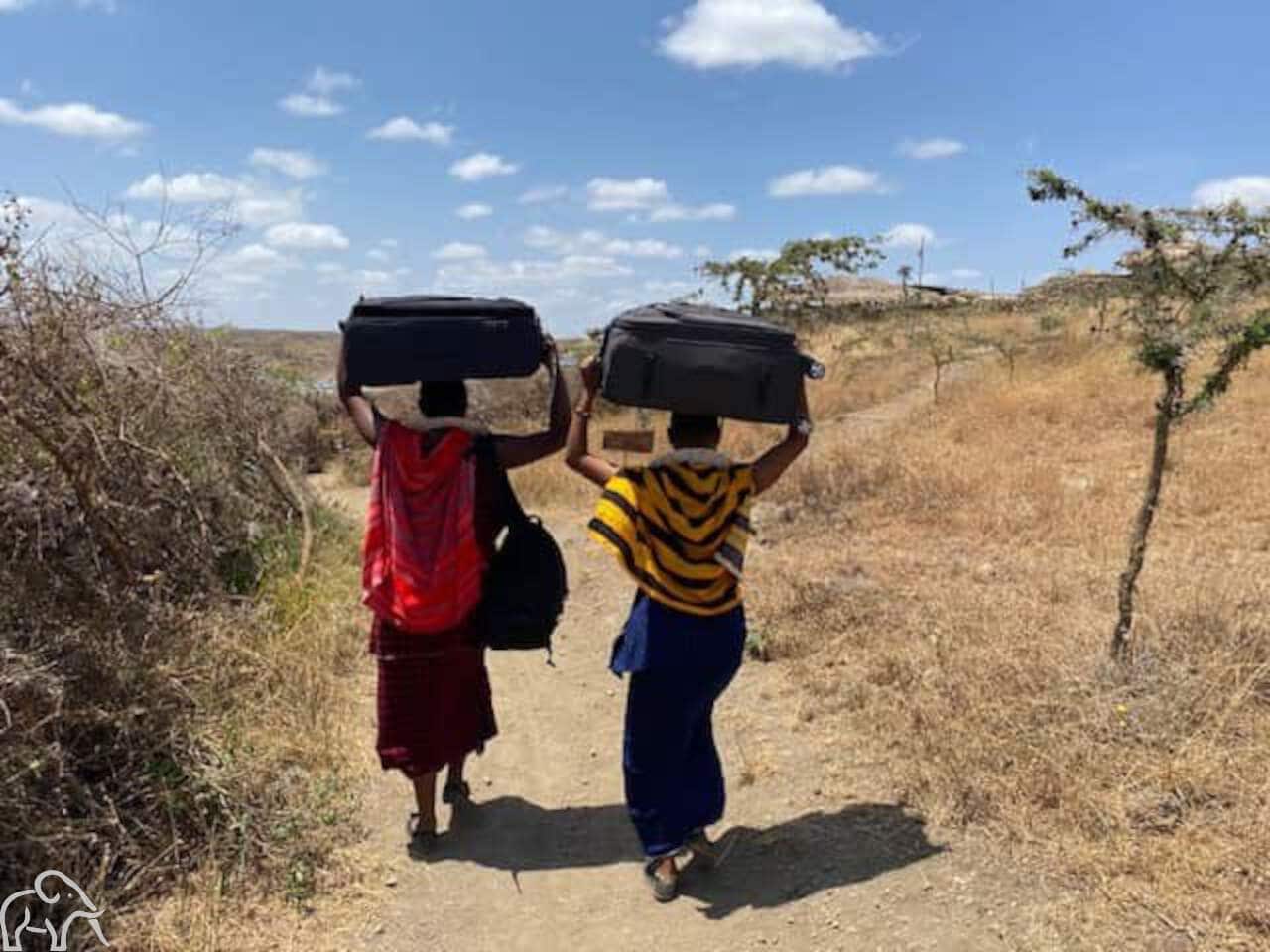 Twee mensen metde koffers van gasten op hun hoofd. Safari Tanzania