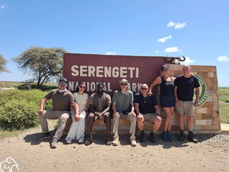 Een groep lachende reizigers zit op het welkomstbord van Serengeti National Park, Tanzania