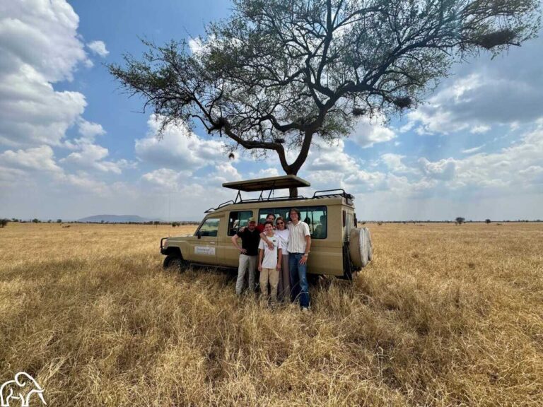 Familie poseert voor hun safariauto onder een grote acaciaboom op de vlaktes van de Serengeti