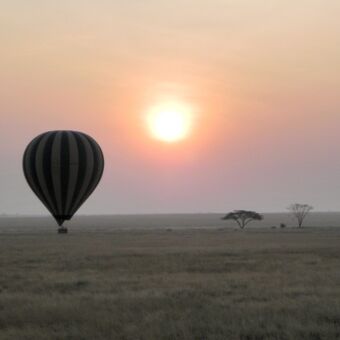 luchtballon laagvliegend over de serengeti met daarachter de zon die opkomt