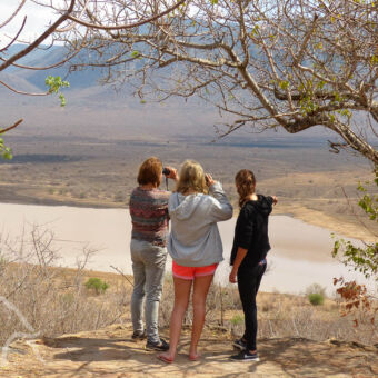panoramisch uitzicht drie vrouwen op een heuvel kijkend en wijzend over Mkomazi landschap met een meertje