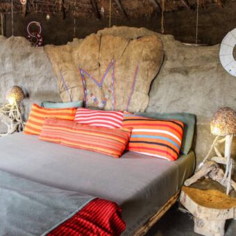 Opgemaakt traditioneel bed mooi gedecoreerd met felle oranje kussens bij Africa Amini lodge