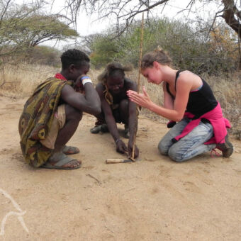 Hadzabe stam jong meisje dat probeert samen met twee mannen van de hadzabe stam vuur te maken met een stokje