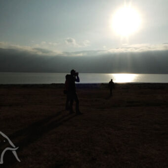 man met kamera in de empakai krater tijdenseen zonsondergang met de zon spiegelend in het krater meer