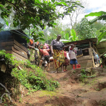 vriendelijke locals vrouw in traditionele kleding met kinderen die gek doen bij houten huisjes in de omgeving van Materuni waterval tanzania