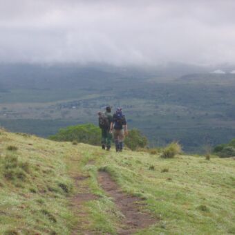 twee mensen lopend licht bepakt in een groen heuvellandschap bezig met de beklimming van Mount Menu tanzania