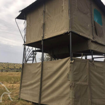 rechtstreeks aan de rivier canvas tentdoek in vierhoeken met een trappetje naar boven waar zich een canvasten bevindt dit alles is gebouw op en aan een landrover dicht bij de mara rivier in de serengeti