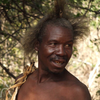 man met een tooi van een baviaan lachende hadzabe man met traditioneel kapsel wat uitstaat naar alle kanten