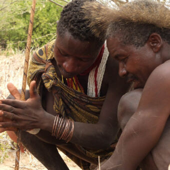 vuur maken met stokjes twee hadzabe mannen die een stok heel snel rond draaien om zo vuur te maken