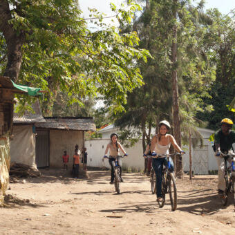 door de dorpjes 2 jonge meiden lachend op de mountainbike samen met een gids fietsend over een onverharde weg door een dorpje